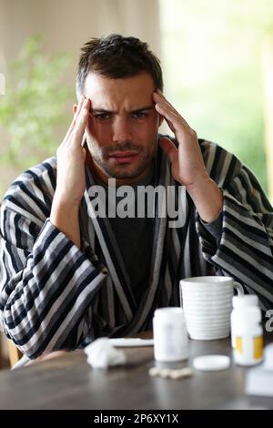 Ha un mal di testa per gentile concessione di congestione. Ritratto di un malato circondato dalla medicina strofinando i suoi templi nel dolore. Foto Stock