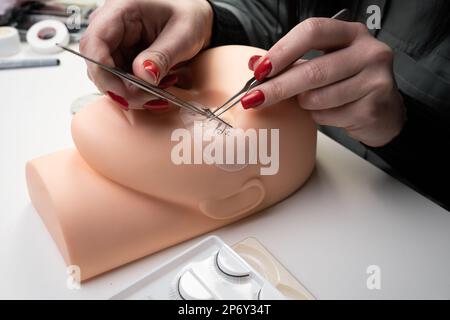 Formazione delle estensioni del ciglia. Lavora con pinzette e ciglia da colorare su una testa di manichino, primo piano. Foto Stock