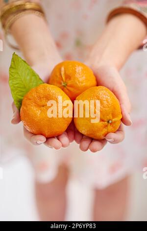 Assaggiate alcuni gustosi tangerini. tre tangerini in mani femminili. Foto Stock