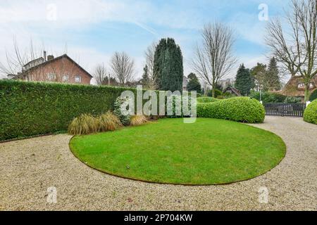 un giardino circolare nel mezzo di una proprietà residenziale con alberi e cespugli che la circondano in una giornata di sole Foto Stock