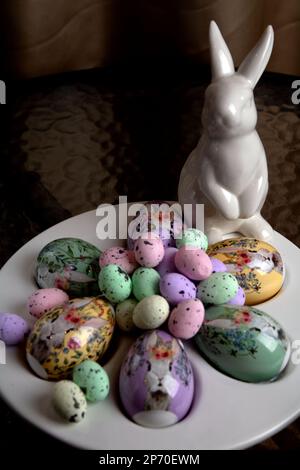 fotografa molte uova decorative colorate di diverse dimensioni e un coniglio bianco in piedi su un tavolo di vetro rotondo Foto Stock