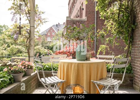 un tavolo e sedie su un patio con fiori in vasi accanto al tavolo è un vecchio edificio in mattoni Foto Stock