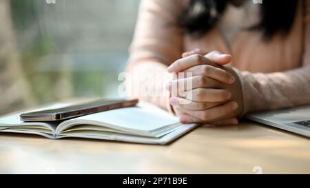 Immagine ritagliata, Una giovane asiatica premurosa e stressata le stringeva le mani insieme sul tavolo. pensare e prendere decisioni gesto mano. Foto Stock
