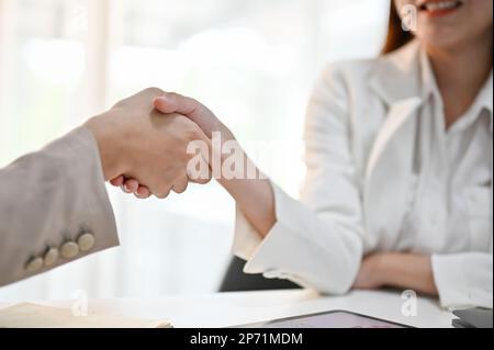 Immagine ravvicinata di due dipendenti di uffici asiatici millenari che si stringono le mani durante la riunione. congratulazioni, benvenuto a un nuovo dipendente. Foto Stock