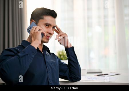 Serio e premuroso uomo d'affari asiatico o capo maschio avere una seria telefonata con il suo cliente in ufficio. Foto Stock