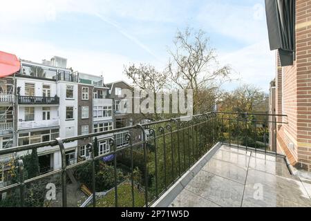 un balcone con alcuni edifici sullo sfondo e un ombrello rosso sospeso da una finestra aperta in una giornata di sole Foto Stock