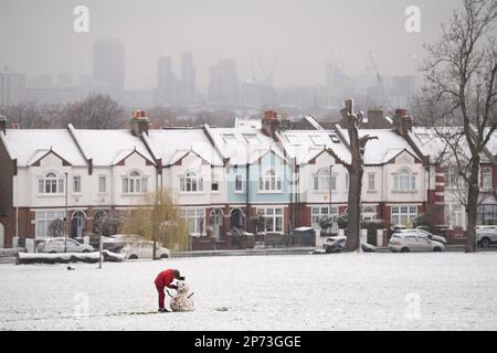 Quando la neve di marzo cade a sud di Londra, un ragazzo costruisce un piccolo pupazzo di neve di fronte alle case d'epoca, a Ruskin Park, uno spazio verde pubblico a Lambeth, il 8th marzo 2023, a Londra, Inghilterra. Foto Stock