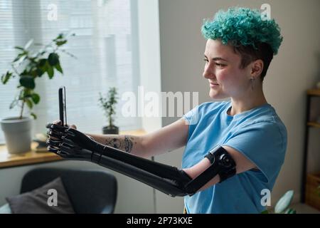 Giovane blogger con braccio protesico utilizzando smartphone per parlare con i suoi seguaci durante la trasmissione online Foto Stock