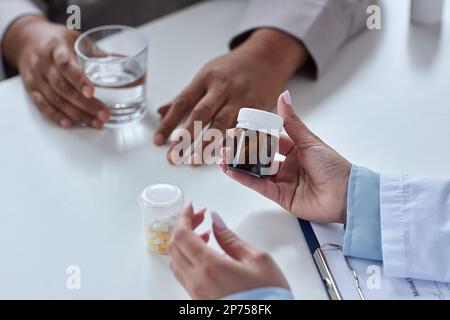 Primo piano della dottoressa che tiene una bottiglia di pillole e spiega il farmaco al paziente in clinica Foto Stock