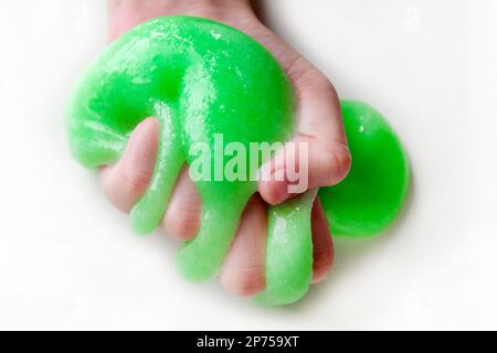 Giocare a mano con texture slime con bolle, stretching la sostanza gooey. Mano adolescente femmina che tiene verde brillante slime, schiacciandolo. Adorabile Gi Foto Stock