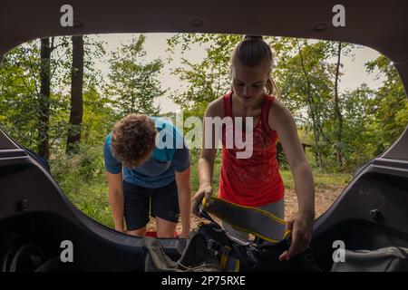 Giovane arrampicatore maschio e femmina che prende l'attrezzatura di arrampicata dal bagagliaio dell'auto e mette le imbracature sopra. Foto Stock