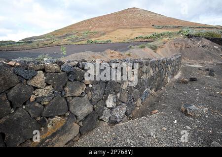 Muro di pietra a secco in pietra vulcanica in costruzione al bordo di un campo vicino a un vulcano a Lanzarote, Isole Canarie, Spagna Foto Stock