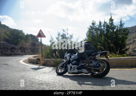 Motociclista che si inclina in una svolta su una strada tortuosa con il cartello di caduta rocce Foto Stock