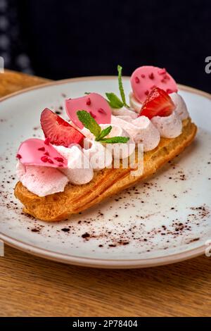 Eclairs con panna e fragole su un piatto bianco. primo piano sul tavolo, serve in un ristorante, menu concetto di cibo. Foto Stock