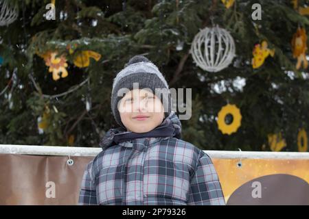 Inverno vicino a un albero di Natale sulla strada si trovava un ragazzo felice in una giacca grigia Foto Stock