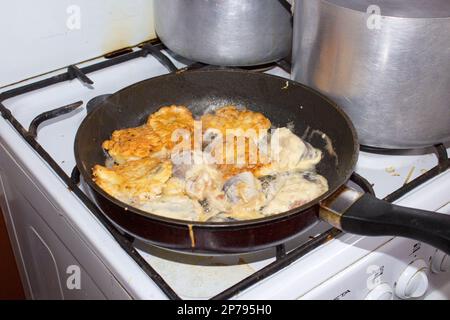 Cuocere il pesce friggere in una padella in cucina Foto Stock