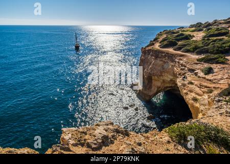 Barca a vela sull'Oceano Atlantide, scogliere e arco sulla costa dell'Algarve, a sud del Portogallo Foto Stock