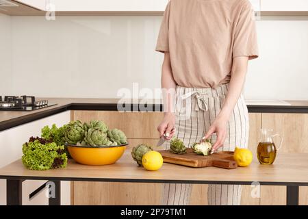 Donna in cucina che si prepara a cucinare i carciofi. Cibo salutare di stagione, vista ravvicinata. Foto Stock
