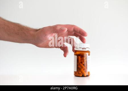 Mano maschio caucasica che raggiunge fuori per afferrare una bottiglia di plastica pillole mediche primo piano shot isolato su bianco. Foto Stock