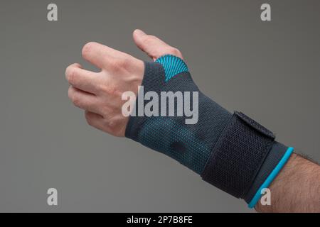 Stabilizzatore di polso in velcro calco indossato da una mano maschio caucasica. Un rinforzo spaccato blu ha significato aiutare la sindrome del tunnel del Carpel. Primo piano scatto in studio, isolato su gr Foto Stock