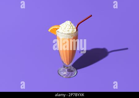 Bicchiere di milkshake arancione sormontato da panna montata minimalista su un tavolo viola. Singolo bicchiere di milkshake in luce brillante isolato su un vivace colo Foto Stock