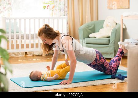 Giovane madre che lavora a casa su un tappetino con il bambino. Interno di un accogliente stanza del vivaio soleggiato. Donna che pratica yoga insieme al bambino. Foto Stock