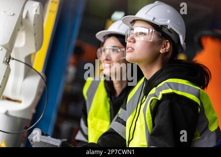 Un team di ingegneri femminili si riunisce per ispezionare i robot di saldatura dell'acciaio controllati dal computer. Pianificare le prove e l'installazione per l'uso. Foto Stock