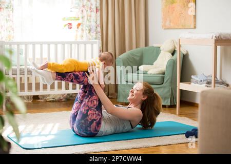 Giovane madre che lavora a casa su un tappetino con il bambino. Interno di un accogliente stanza del vivaio soleggiato. Donna che pratica yoga insieme al bambino. Foto Stock