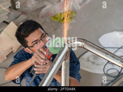 I lavoratori utilizzano il macinacaffè per lucidare. Vernice in acciaio inox in cantiere. Foto Stock