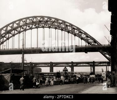 Commercio dal 1736: Il mercato domenicale di Quayside all'ombra del ponte ad arco di Tyne che collega Newcastle upon Tyne a Gateshead in Tyne e Wear, Inghilterra, Regno Unito. Questa immagine monocromatica vintage è stata ripresa nel 1950. Foto Stock