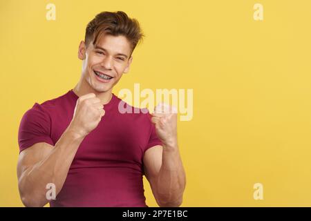 Uomo con le staffe che festeggia con i pugni sollevati Foto Stock