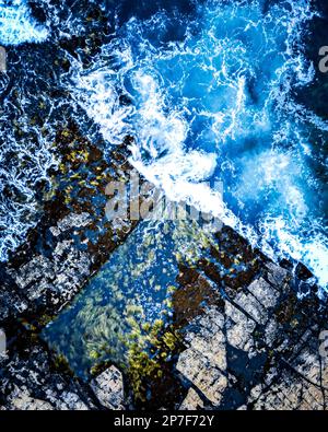 Una scena drammatica di onde potenti che si infrangono contro la costa rocciosa Foto Stock