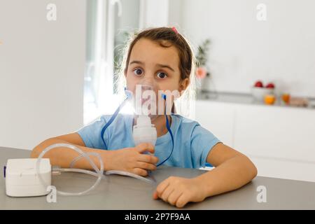 Bambina in una maschera, trattamenti del tratto respiratorio con un nebulizzatore a casa Foto Stock