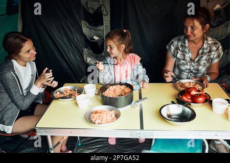 Famiglia che ha la colazione all'aperto in campeggio durante le vacanze estive. Pane, formaggio di ricotta, carne fredda, pomodori, frutta e tazze di caffè sul tavolo. Chiudi Foto Stock