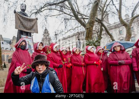Le donne anglo-iraniane che protestano vestite come i personaggi del racconto dell'Annua in occasione della Giornata internazionale delle donne del 2023 si trovano sotto una suffragetta. Foto Stock