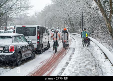 Ciclisti che camminano a piedi tenendo biciclette su strade scivolose / sentiero coperto di slittino durante inaspettata doccia sulla neve tarda nel mese di marzo, Gent, Belgio Foto Stock