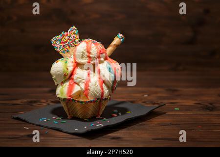 gelato alla vaniglia in cialde con salsa di frutti di bosco, spolverati e sigari decorati e ventilatori versati con glassa di cioccolato su fondo di legno Foto Stock