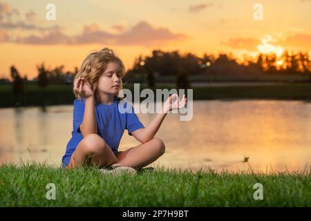 Il bambino pratica yoga e medita nella posizione del loto vicino al lago. Foto Stock