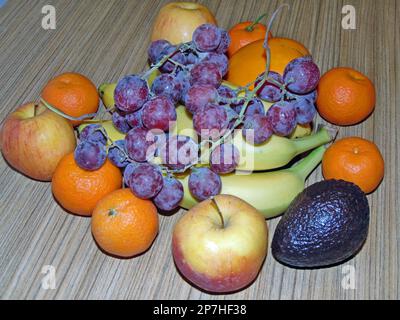 frutta su un fondo di legno - clementine, persimmon, mele, mela, banane, avocado, uva rosa Foto Stock