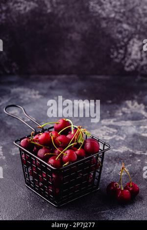 Ciliegie rosse dolci fresche nel cestello su fondo scuro, fuoco selettivo Foto Stock
