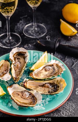 Ostriche fresche aperte su un piatto blu, servite con limone e ghiaccio. Foto Stock
