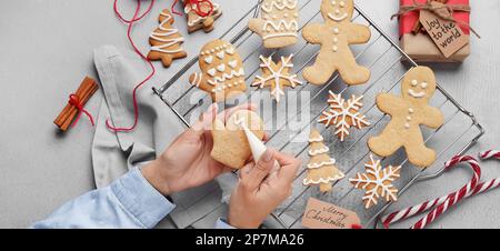Donna che decorano biscotti di pan di zenzero di Natale su sfondo chiaro, vista dall'alto Foto Stock