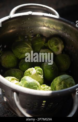 Germogli verdi di Bruxelles freschi e puliti in vecchio colino metallico con gocce d'acqua. Messa a fuoco selettiva. Reale cucina candida stile di vita sfondo Foto Stock