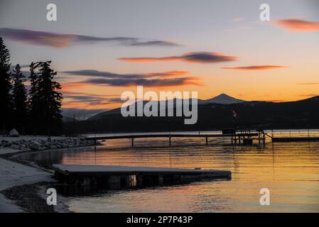 Splendido tramonto autunnale su un lago selvaggio con attracco per barche nel nord del Canada durante la stagione autunnale. Montagna innevata in lontananza. Foto Stock