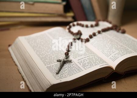 Primo piano di una bibbia aperta in cima alla quale si trova un crocifisso in legno e metallo, con altri vecchi libri sullo sfondo sfocato Foto Stock