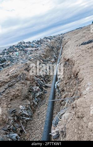 Un tubo perforato per gas metano viene posato in una trincea per essere interrato in una discarica attiva. Foto Stock