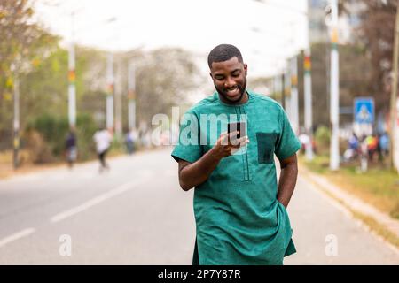 Giovane uomo africano sicuro di usare lo smartphone all'aperto, esperto di tecnologia che esplora nuove applicazioni sul telefono Foto Stock