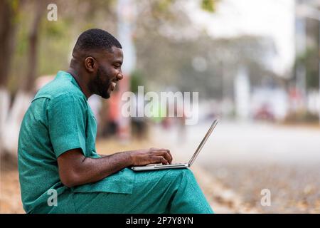 Un giovane imprenditore africano con un notebook all'aperto parla con i clienti in remoto, istruisce i clienti sulla sicurezza informatica. Foto Stock