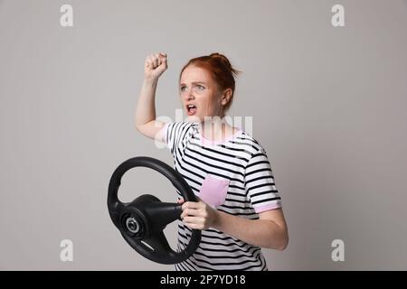 Giovane donna emozionale con volante su sfondo grigio Foto Stock