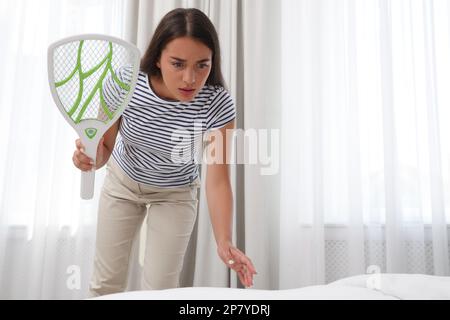 Giovane donna con mosca elettrica swatter in camera da letto. Insetto killer Foto Stock